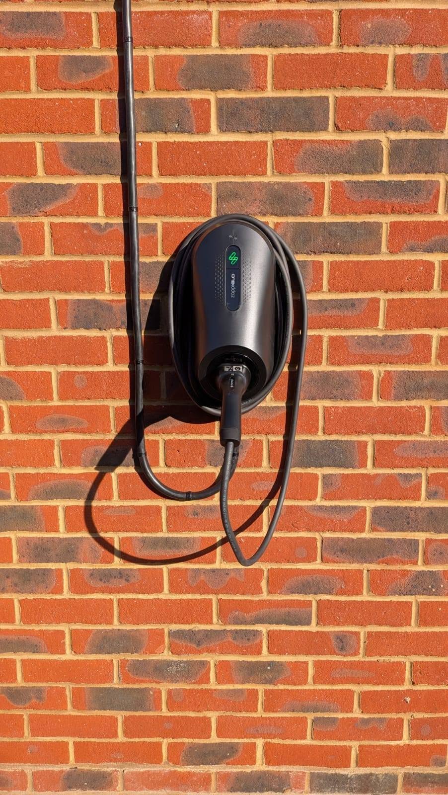 Close-up of a black Zappi home EV charger mounted on brickwork.