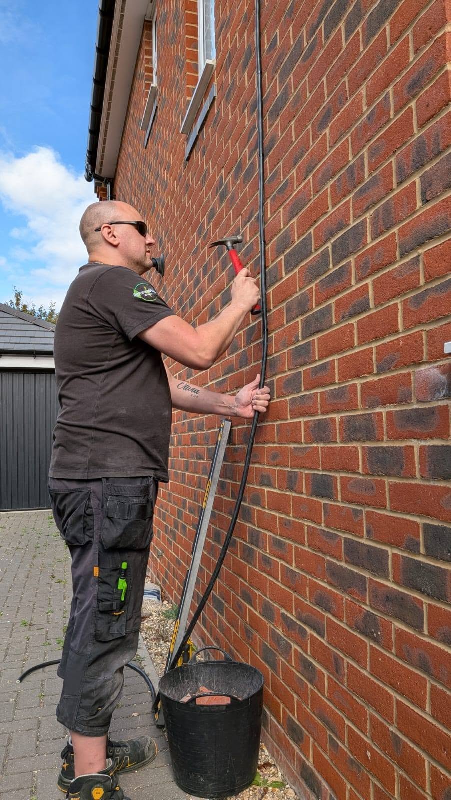 Installer positioning a cable and preparing a brick wall for a Zappi EV charger.