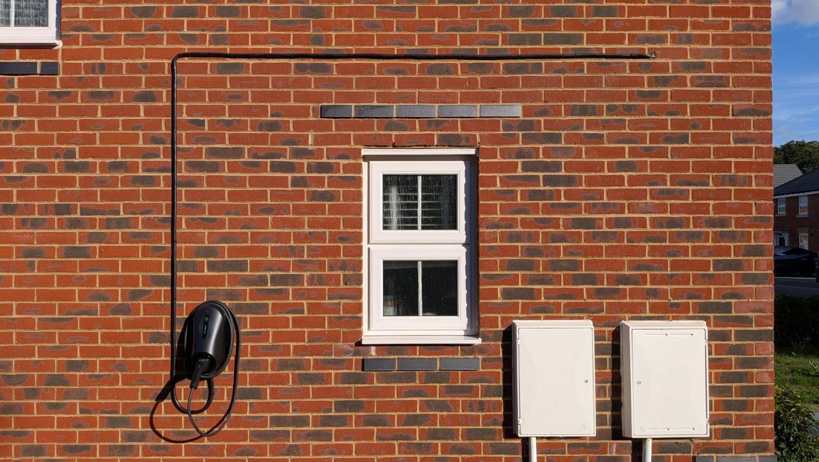 Black Zappi home EV charger mounted on a red brick wall with its cable in place.