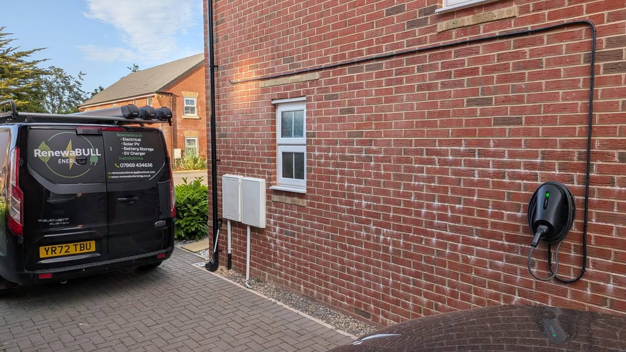 A black EV charging unit mounted on a red brick wall beside electrical enclosures.